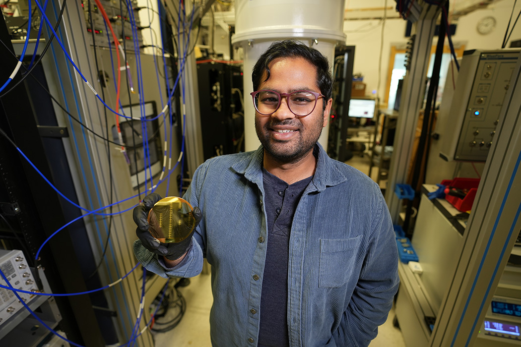Akash Dixit stands in the lab surrounded by server racks and wiring, holiding a reflective disk. 
