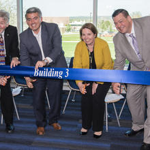 Four people with scissors get ready to cut a blue ribbon that says "Building 3" on it