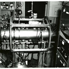 Man standing behind a big horizontal cylinder of metal and a lot of wires