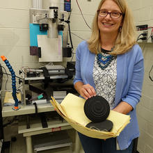 Woman stands in a lab holding two black round disks