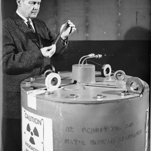 A man in a suit stands next to a large metal tank.