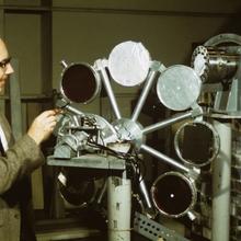 A man in a suit stands next to a piece of equipment with round targets.