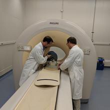 Two men in lab coats stand beside a large scanner