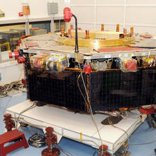 Workers in protective suits construct a large orbital satellite