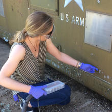 Woman in safety goggles handles an instrument with a thin metal tube at the end.