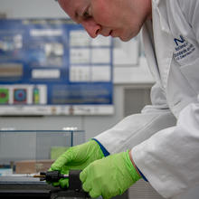 Man in lab coat leans over bullet in holder.