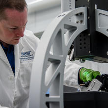 Man in lab coat reaches under microscope to place sample.