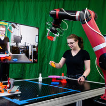 Engineer in a lab. Screen that shows her face on the left. On the right is a robot.