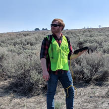 A man in a high-visibility vest (Jordan O'Dell) stands outside holding a black device.