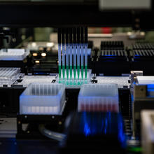 A row of eight pipettes suck up green liquid before moving it to a different set of wells for testing.