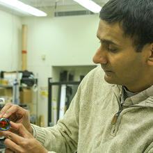 man in a lab adjusting a small metallic ball with a mirror in it attached by a magnet to a large swinging metal arm