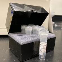 An open black box with foam inserts holds plastic vials labeled SRM 2917.