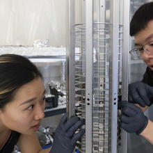 Two researchers examine a cylindrical metal device used to trap ions.