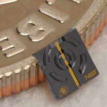 A tiny black chip with NIST and CU Boulder logos leans against a dime for size. 
