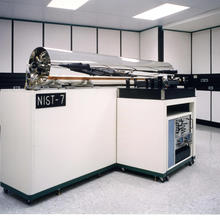 A large shiny silver-colored cylinder is mounted on white cabinetry with a sign saying "NIST-7."