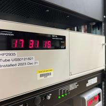 A tan rectangular box with a digital readout (17 31 15) sits on a server rack. 