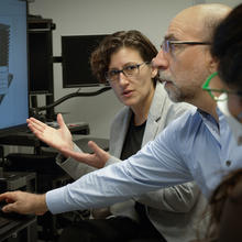 A woman gestures to a building model on a computer screen as she speaks to the two other researchers sitting near her. 