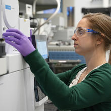 Briana Capistran wears safety glasses and purple gloves as she operates laboratory equipment. 