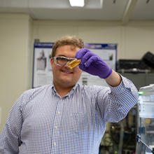 Peter Beaucage stands in the lab holding up a vial of yellowish liquid. 