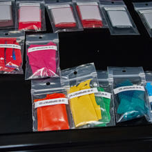 Different colored clothing samples are labeled and held inside plastic pouches inside a cabinet drawer in a lab.