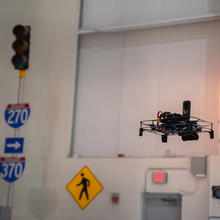 UAS in air inside a testing facility that includes street signs and stoplights. 
