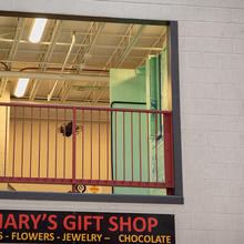 A drone is flying inside a second-story balcony space in a testing facility that includes pretend storefronts like Mary's Gift Shop. 