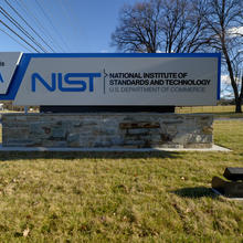 Outdoor sign with trees and telephone wires in background reads: NIST: National Institute of Standards and Technology: Gate A
