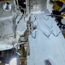 Close-up view of connection point shows concrete beam broken away from slab and exposed rebar.