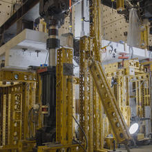 Horizontal concrete slab is visible in a forest of scaffolding and equipment in a large indoor space. 