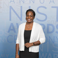 Melissa Taylor poses smiling in front of a banner for the NIST Awards Ceremony.