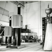 Historical photo shows a large lab space with cylindrical metal towers of different shapes. 