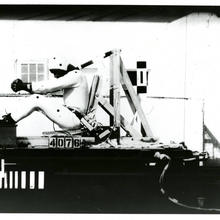 Historical photo shows test subject in helmet and bodysuit strapped into moving seat.