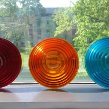 Three round colored lenses are displayed on a window ledge: red, orange and blue. 