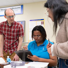 Tobias Herman, Instructor, collaborates with students attending a “Fundamentals of Metrology” course as they perform measurements in the Office of Weights and Measures Training Laboratory, Gaithersburg, Maryland.