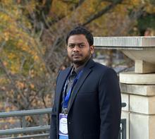 Man wearing a dark suit standing by trees in the fall season