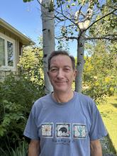 man outside near trees and bushes wearing a blue tee shirt