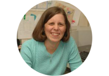 person with shoulder-length brown hair and a light blue blouse, sitting at a desk