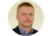 person with very short dirty blond hair and a beard, wearing a suit jacket and dress shirt