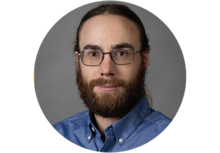 person with a dark brown beard and a ponytail wearing glasses and a dress shirt
