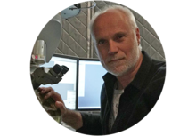 person with short white hair and a short white beard, working with a scientific instrument