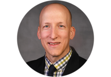 a smiling person with a bald head, wearing a suit and tie