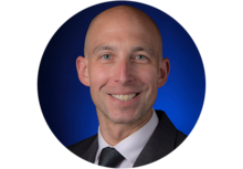 Headshot of Gabriel Swiney, a bald man wearing a suit and tie in front of a blue background