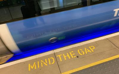 image of a subway train as it rushes past, the words "mind the gap" appear on the subway platform