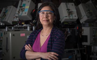 Joannie Chin stands with arms crossed, wearing safety goggles, in front of scientific equipment. 