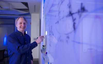 Alexey Gorshkov poses at a whiteboard, holding a marker. 