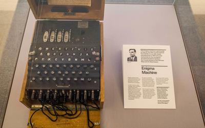 Left: Machine that looks like an old fashioned typewriter in a box. Right: picture of Alan Turing along with a bio. Both are from a museum exhibit.