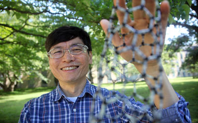 Ming Zheng stands outside smiling and holding a model of a nanotube made of a lattice of smaller tubes.