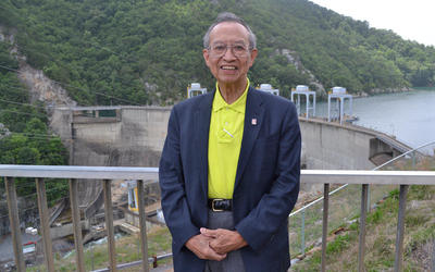 Jeffrey Fong poses smiling in front of a railing overlooking a concrete dam. 