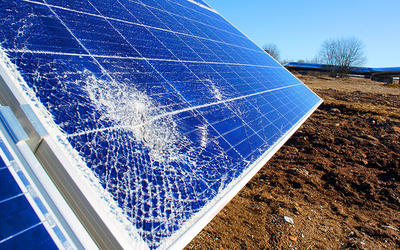 A ground-mounted solar panel has a spiderweb crack in the lower left-hand corner. 