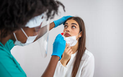 A medical worker wears gloves as she prepares to swab the nose of a female patient. 